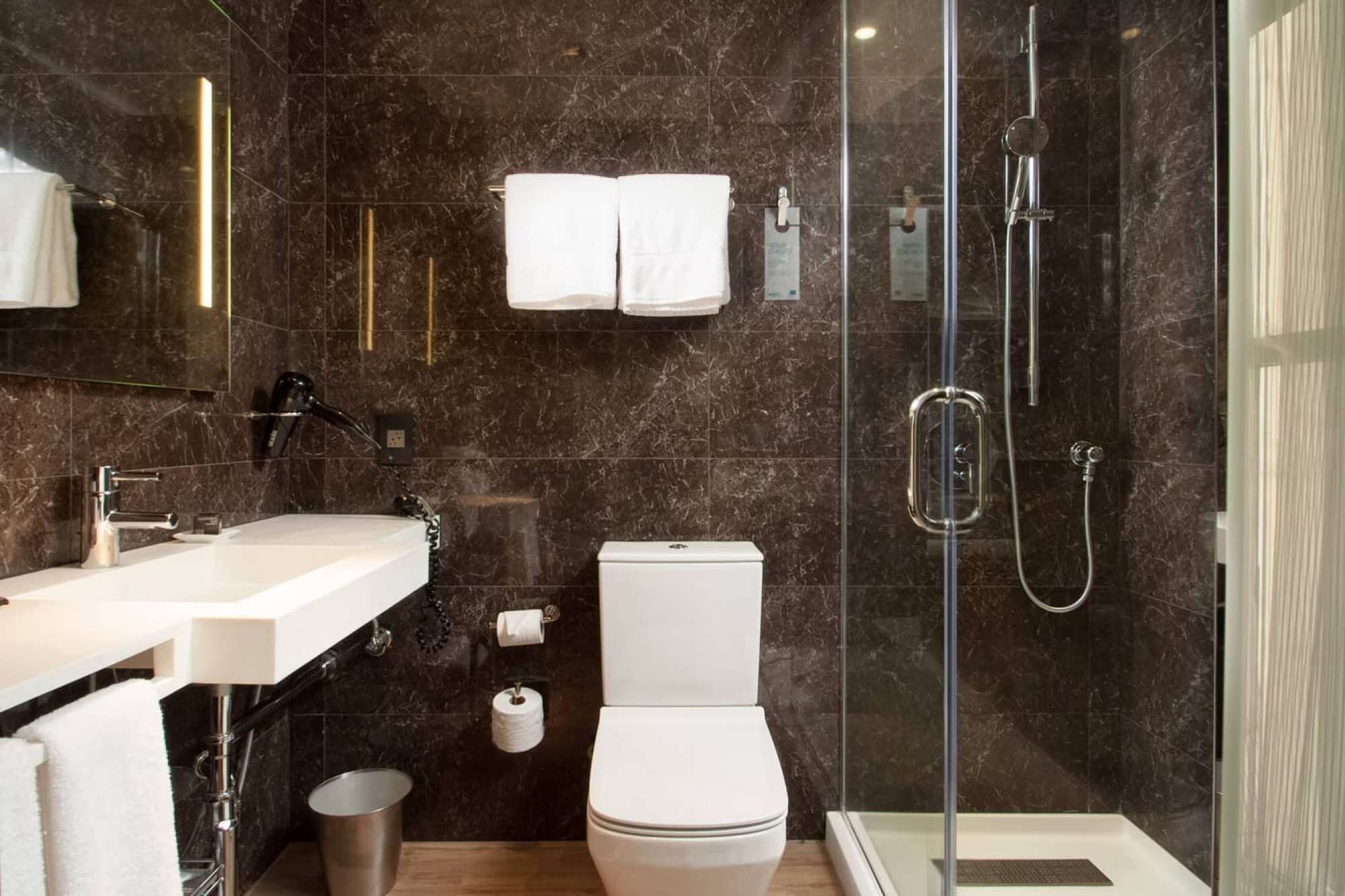 Une salle de bain moderne avec une douche à parois de verre, des toilettes blanches et un meuble-lavabo à deux vasques.