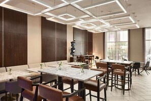 Un comedor moderno con mesas de mármol, sillas de cuero e iluminación de techo geométrica.