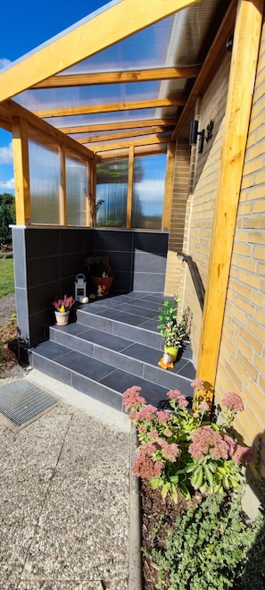 A covered outdoor area with a wooden roof, black tiled steps, and potted plants. - Cozy vacation apartment in a quiet location with garden and terrace (Schwienau)