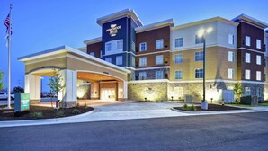 Ein mehrstöckiges Hotel mit modernem Design, das einen markanten Eingangsbereich mit überdachtem Gang und einer Fahnenstange zeigt.