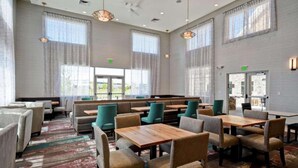Ein geräumiges Restaurant mit hohen Decken, großen Fenstern und verschiedenen Sitzgelegenheiten, darunter Essecken und Tische.