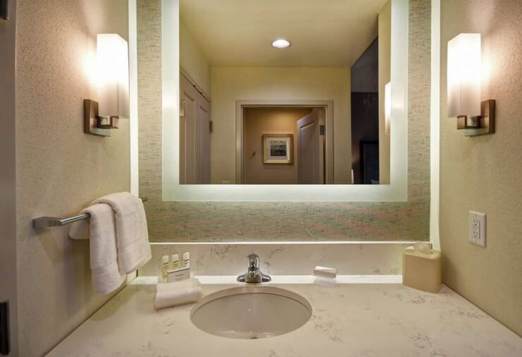 A bathroom with a large mirror, a sink, and two wall-mounted light fixtures.