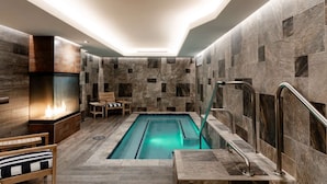 Un área de piscina interior moderna con una piscina rectangular, paredes de piedra y un banco de madera.