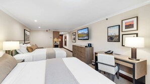 Une chambre d’hôtel avec deux lits, un bureau, une chaise, une télévision et des œuvres d’art accrochées aux murs.