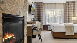 Una habitación de hotel con chimenea, un escritorio con silla, una cama y un televisor montado en la pared.