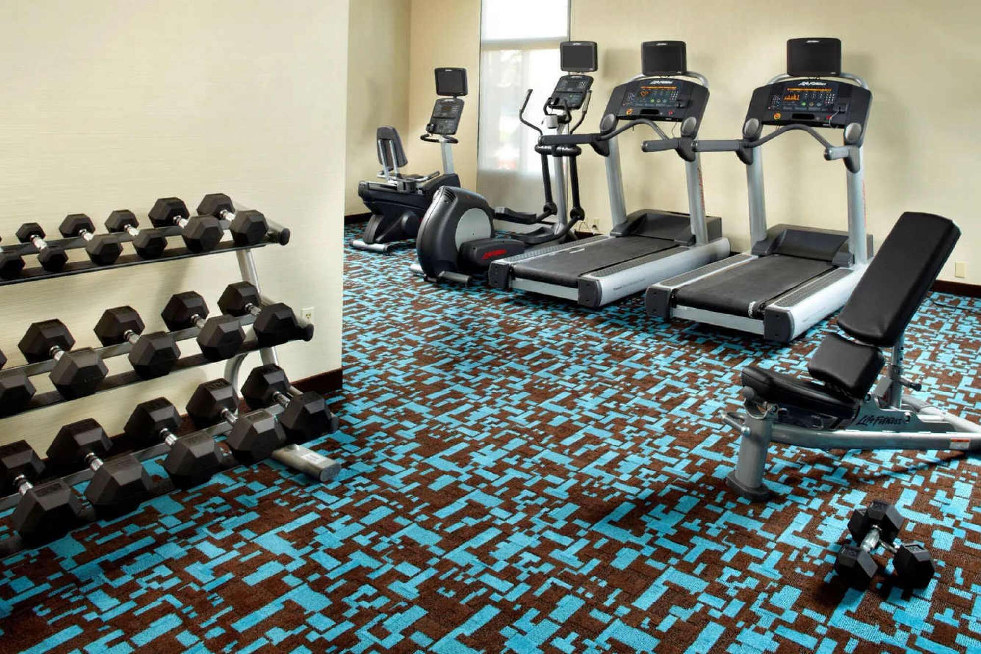 Un gimnasio con mancuernas, cintas de correr y un banco.