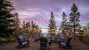 En sittplats med Adirondack-stolar som är placerade så att man har en vacker utsikt över träd och en sjö eller ett annat vattendrag.