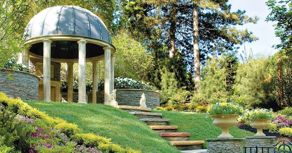 A gazebo with columns, surrounded by a garden with steps leading up to it.