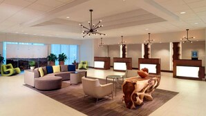 A spacious lobby with a modern design, featuring a sectional sofa, a round wooden coffee table, and a reception desk with a digital display.