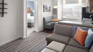 A modern hotel room with a gray sofa, a small round table, a painting on the wall, and a view through a window. - Near Flatiron Crossing + Free Breakfast & Pool (Broomfield)