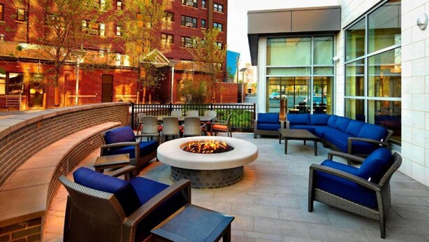 Une terrasse extérieure avec des meubles en osier, un foyer central et un mur en briques.