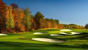 Un parcours de golf avec des bunkers de sable et des arbres aux couleurs automnales.