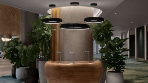 A modern lobby with a central wooden reception desk, multiple potted plants, and a unique cylindrical light fixture. - By Gas South Convention Center + Rooftop Bar. Pool (Duluth)