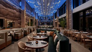 A spacious indoor dining area with multiple seating options, including round tables and sofas, and a central bar area. - By Gas South Convention Center + Rooftop Bar. Pool (Duluth)