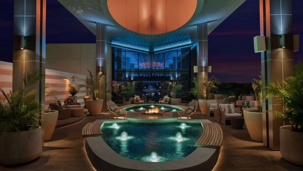 A pool area with a fire feature, seating, and a bar in the background. - By Gas South Convention Center + Rooftop Bar. Pool (Duluth)
