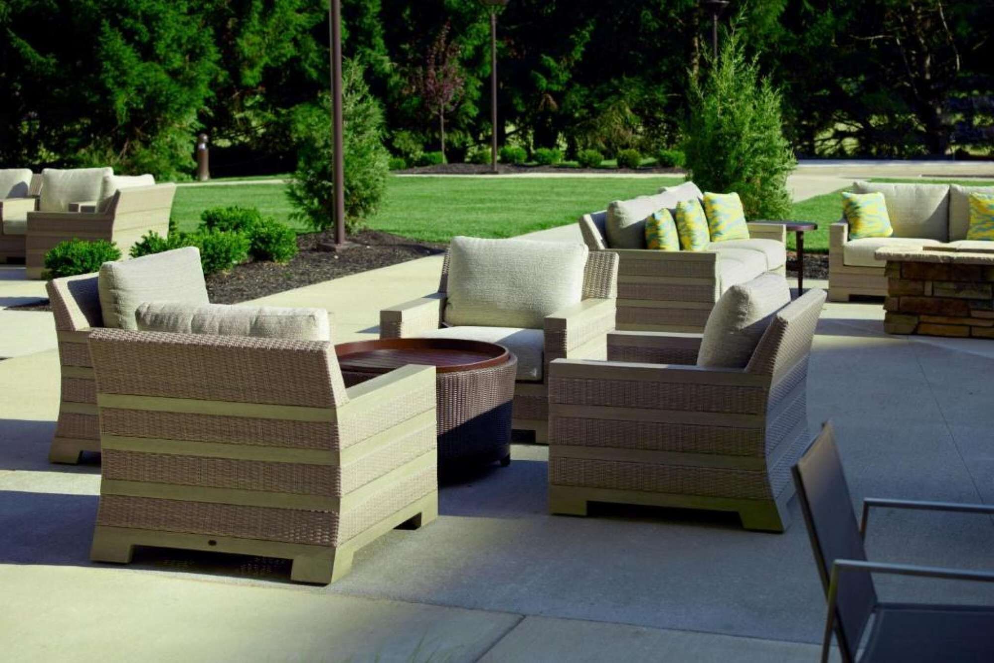 Un patio al aire libre con mobiliario de mimbre, incluyendo sofás y una mesa de centro, dispuesto alrededor de un hogar central.