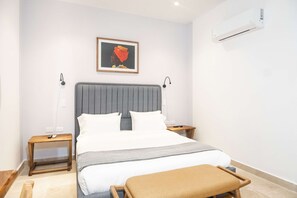 A bedroom with a bed, bedside tables, a nightstand, a bench, an air conditioner, and a framed picture on the wall. - w Designer Loft in the Heart of Bocagrande (Cartagena)