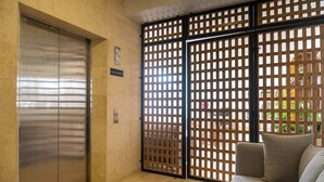 Un hall d’hôtel avec un ascenseur hors service, une cloison en bois et un canapé avec des coussins.