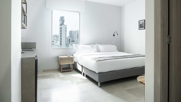 Une chambre moderne avec un grand lit, une table de chevet, une fenêtre donnant sur la ville et une porte.