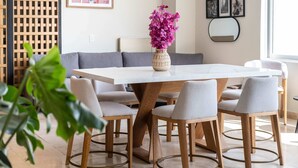 Un coin repas avec une table blanche, six chaises grises et un vase rempli de fleurs roses.