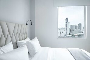 A modern bedroom with a city view, a headboard with headphones, and a neatly made bed. - w Dazzling 2BR in the Heart of Bocagrande (Cartagena)