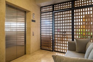 Eine Hotelhalle mit geschlossener Aufzugtür, einer Holzwand und einer Couch mit Kissen.
