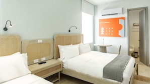 Hotellihuone, jossa on kaksi sänkyä, pieni pöytä ja seinälle asennettu ilmastointilaite.