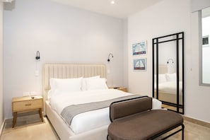 Quarto de hotel com cama, mesas de cabeceira, um banco, espelho e obras de arte na parede.