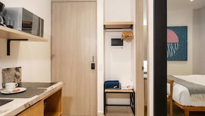 A compact hotel room with a wooden door, a small table with a cup and saucer, a microwave on a shelf, a bed with a blanket, and a wall art piece. - w Awesome Loft in the Heart of Bocagrande (Cartagena)