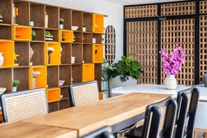 A dining area with a wooden table and chairs, a bookshelf with orange and wooden shelves, and a potted plant with pink flowers. - w Boutique Loft in the Heart of Bocagrande (Cartagena)