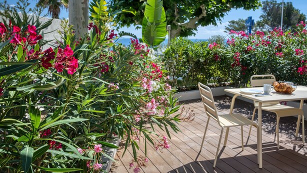 Un patio al aire libre con una mesa y sillas, rodeado de exuberante follaje y plantas con flores.