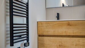 Un baño con un tocador de madera, un perchero, un espejo y una lámpara de pared.