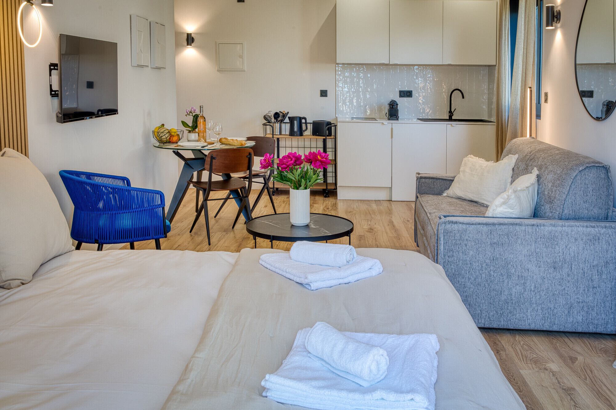 Ein modernes Hotelzimmer mit einem Bett, einem grauen Sofa, einem Essbereich mit Tisch und Stühlen sowie einer Küchenzeile.