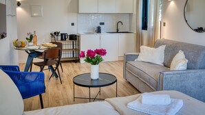 Un espacio habitable compacto con kitchenette, zona de comedor y área de estar con sofá y sillón.
