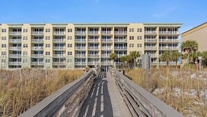 A multi-story hotel with balconies, a wooden boardwalk leading to the entrance, and a beachside view. - Waters Edge 115 ~ Ground Floor ~ Beach Boardwalk Right Outside Your Door! (Fort Walton Beach)
