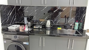 Una cocina compacta con lavadora, cafetera y hervidor.