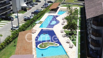 Una piscina con un diseño singular, rodeada de un estacionamiento y edificios colindantes.