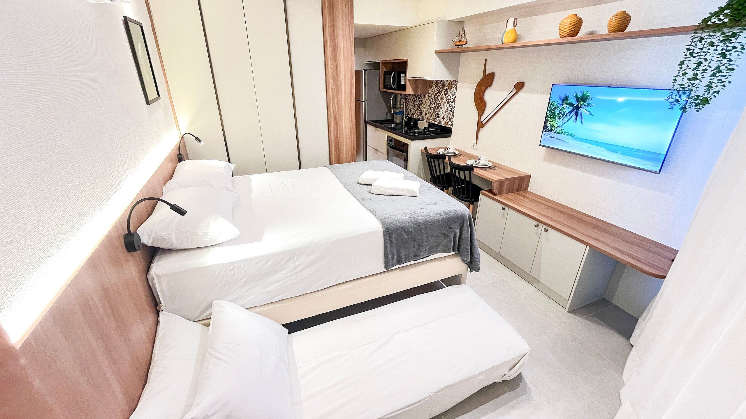 A compact hotel room with two beds, a kitchenette, a TV, and a small dining area.