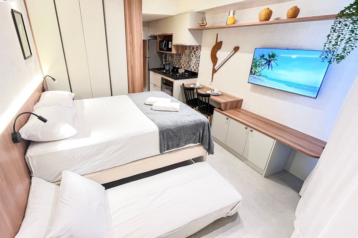 A compact hotel room with two beds, a kitchenette, a TV, and a small dining area.