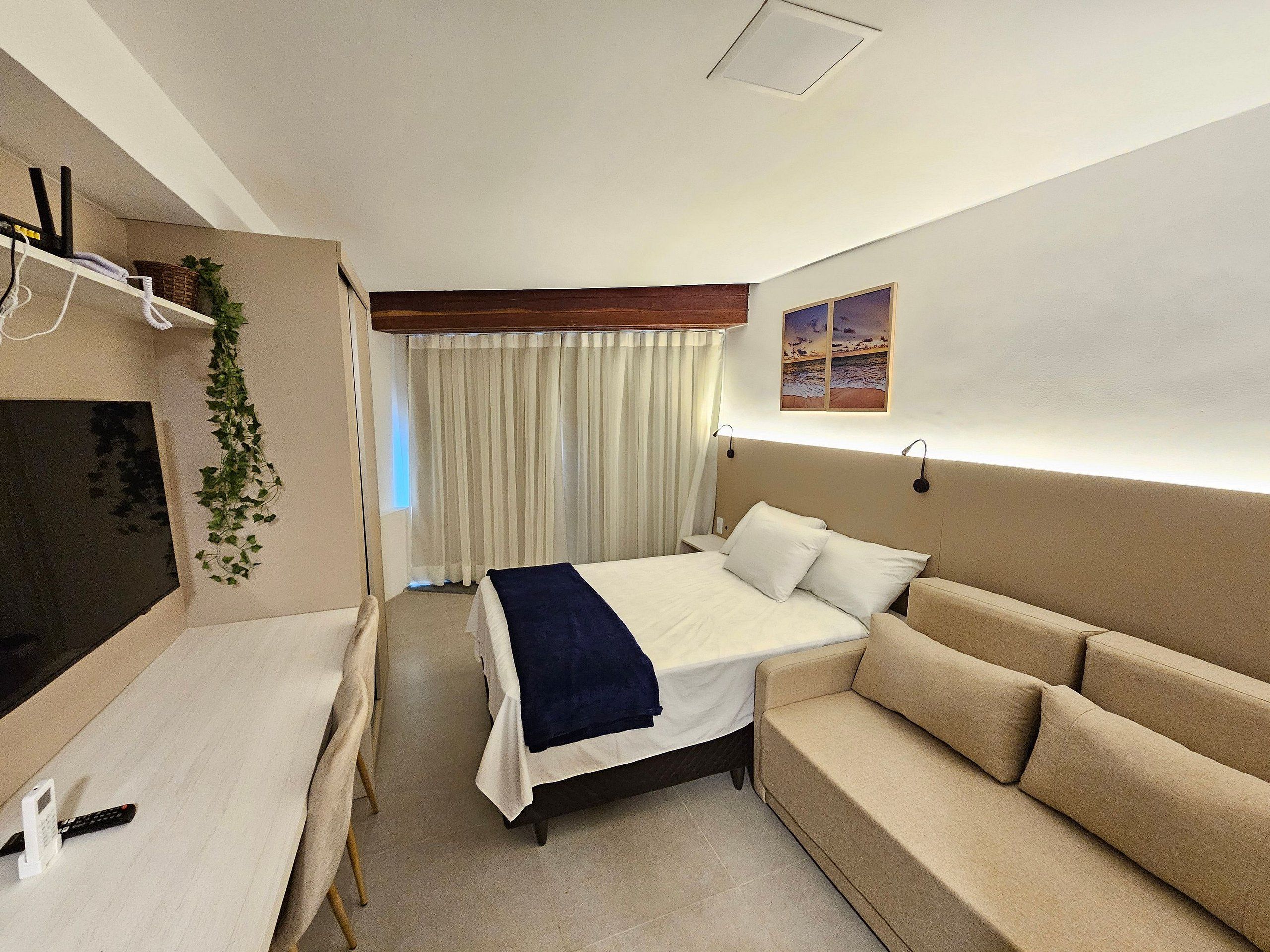 Een hotelkamer met een bed, een bank, een televisie, een bureau en een gordijn.