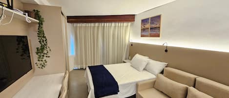 Een hotelkamer met een bed, een bank, een televisie, een bureau en een gordijn.