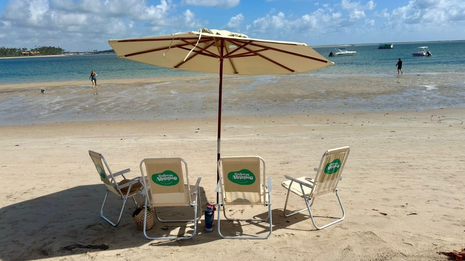 A beach with three beach chairs and an umbrella, a clear sky, and boats in the water.