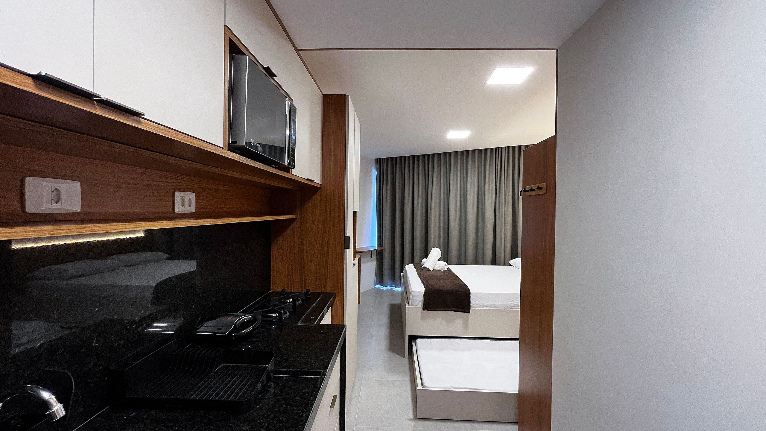 A compact kitchenette with a stove, microwave, and a flat-screen TV mounted above it.