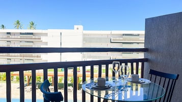 Un balcón con una mesa de vidrio preparada para dos personas, una silla y vistas a edificios modernos.