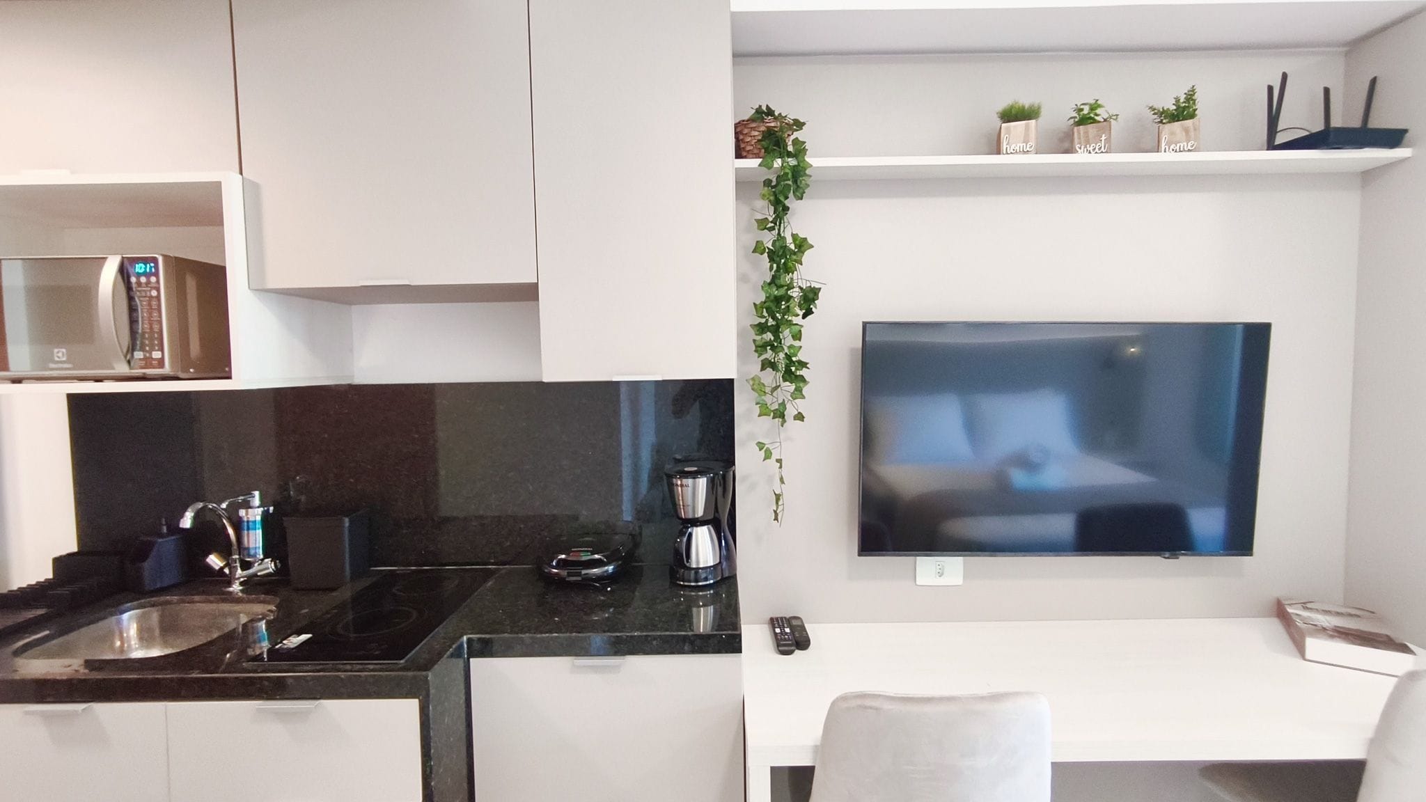 A modern kitchen with a built-in microwave, a coffee maker, and a TV mounted on the wall.