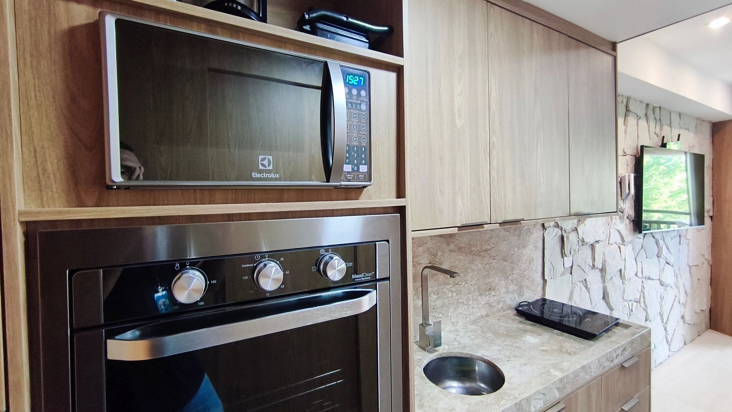 A kitchen with a microwave, oven, and a stone backsplash.