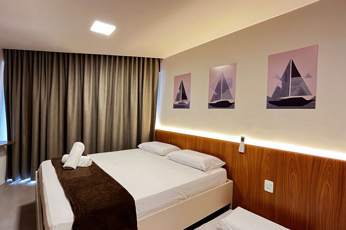 A hotel room with a bed, a bedside table, a wall-mounted phone, and curtains.