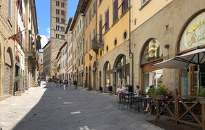 Una calle peatonal bordeada de edificios históricos, con mesas de café al aire libre y un cielo azul despejado.