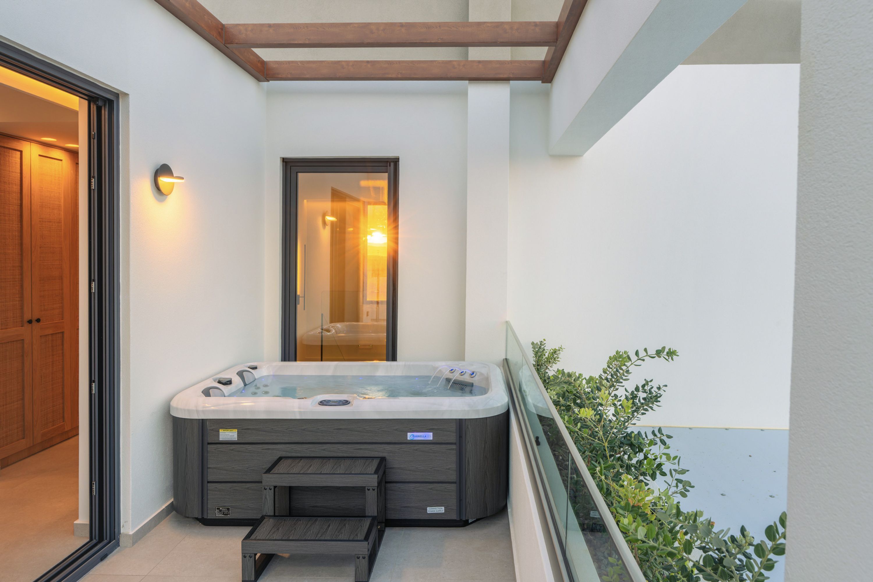 A hot tub in a covered outdoor area with a glass railing and a door leading to an interior space.