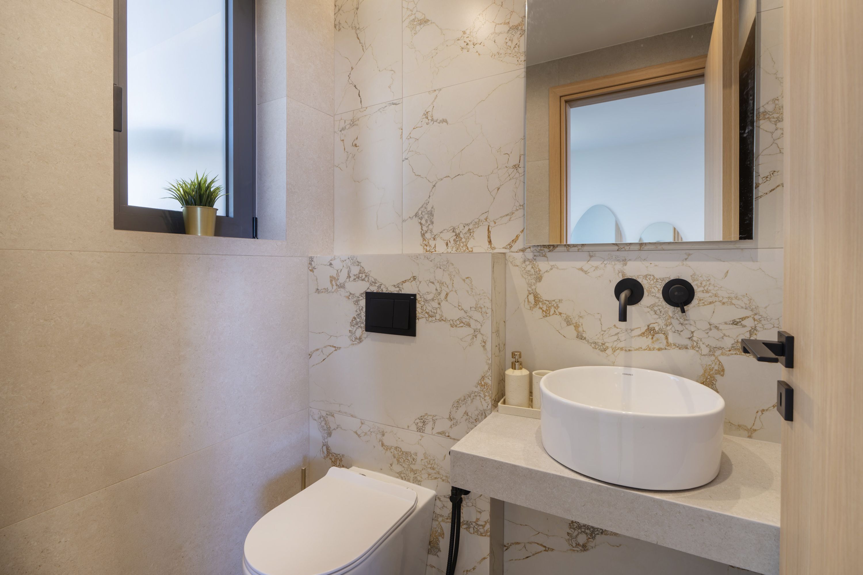 A modern bathroom with a white toilet, a marble backsplash, and a large sink with a mirror above it.